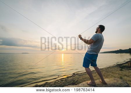man on sand beach looking on sunrise with hands up