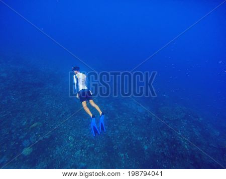 Freediver swims underwater in deep blue sea. Snorkeling man dives up to water surface. Open water diving lesson. Ocean deep open water view. Diver man silhouette undersea photo. Sea landscape view