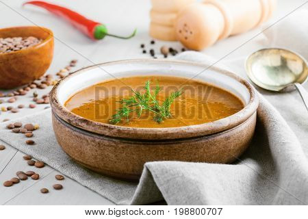 Lentil soup in a rustic bowl on a cotton canvas tablecloth. Healthy vegetarian food on a white wooden table.