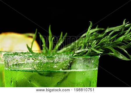 Close-up of delicious and refreshing alcohol beverages with bright spicy tarragon and ice cubes. Fruity cocktail in a tall glass on a black background. Cool drink and a cut juicy melon.
