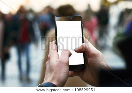 Photo of a man's hands holding phone with blank screen and blurred people in the street in the background