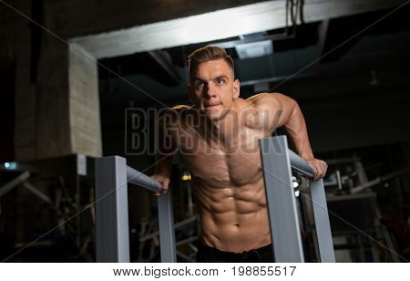 fitness, sport, bodybuilding and people concept - young man doing triceps dip exercise on parallel bars in gym