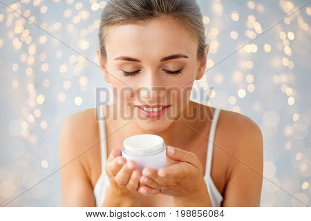 beauty, cosmetics, skin care and people concept - close up of beautiful happy woman holding and smelling cream jar