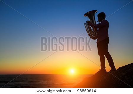 Silhouette of musician play Tuba on sea beach at magical sunset.