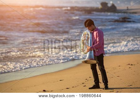 Musician with Tuba on the sea coast during surf. Romantic Instrument. 
