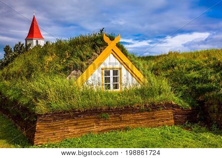The village of houses covered with turf and grass. Church bell tower with red gabled roof. Ethnographic Museum-estate Glaumbaer, Iceland. The concept of the historical and cultural tourism