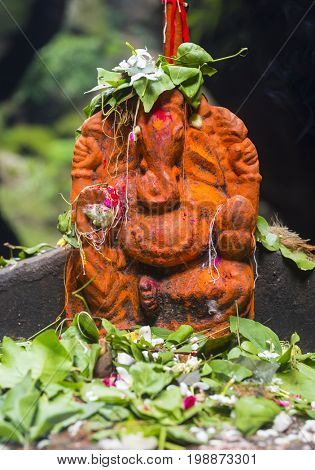 An old, rustic statue of Ganesha in an open temple covered with sacred orange paint.