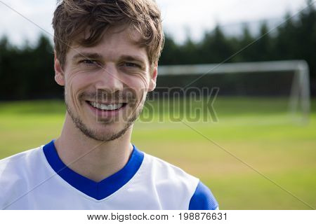 Portrait of smiling male soccer player with arms crossed standing on playing field