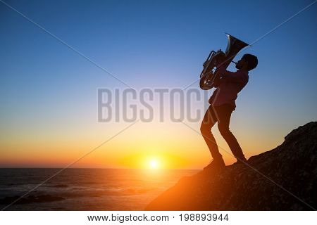 Silhouette of musician play Tuba on sea shore at sunset.