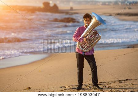 Musician playing the Tuba musical instrument on the sea coast. Romantic.