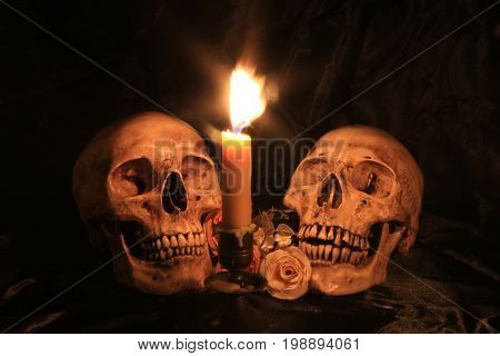 Human Skull With Roses Over Black Fabric Texture Background With Light Candle In Dim Halloween Night