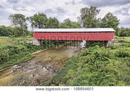 The historic and newly restored Scipio Covered Bridge crosses Sand Creek on a cloudy day in rural Jennings County Indiana.