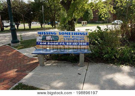 JOLIET, ILLINOIS / UNITED STATES - JULY 17, 2017: Avid Dental P.C. advertises dental services on a public bench at a bus stop on Plainfield Road.