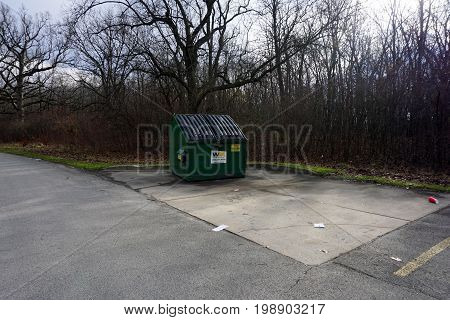 SHOREWOOD, ILLINOIS / UNITED STATES - DECEMBER 6, 2015: A garbage dumpster sits in the corner of a parking lot in the Hammel Woods Forest Preserve.