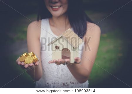 Money Cash And A Model Home In Woman Hands. Young Lady Hands Holding Little House Toy And Pile Of Go