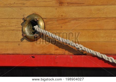 A mooring rope coming out of the hole in the side of the ship. Thick twisted rope.