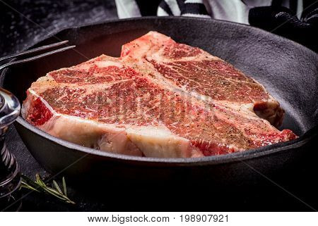 Fresh raw meat t-bone steak in a skillet marinated with herbs and spices shot with a dark background.