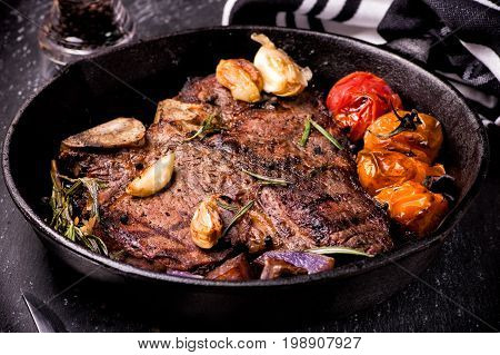 Pan grilled large t-bone steak with garlic tomatoes herbs and seasoning.