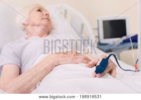 Professional equipment. Worried chronic sick lady recovering from a disease and having her pulse in check all the time while lying in hospital bed