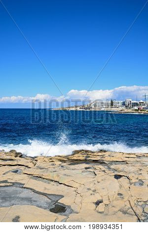 Sea crashing onto the rocky coastline with hotels and apartments to the rear Bugibba Malta Europe.