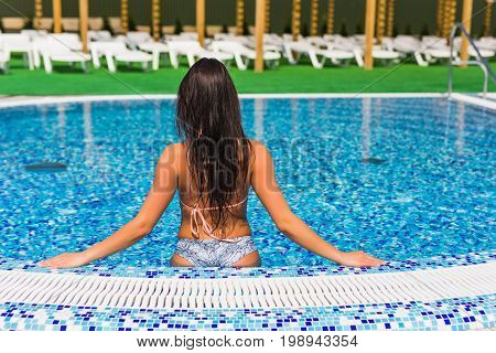 Beautiful Girl In A Bathing Suit Sits On The Edge Of The Pool, The View From The Back