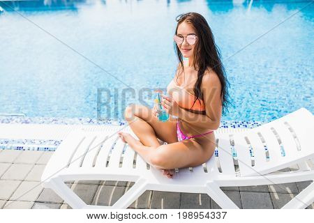 Side View Of Woman Sunbathing By The Swimming Pool And Drink Cocktail