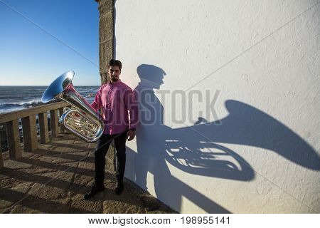 Musician with Tuba near the white wall the shadow of the tool.