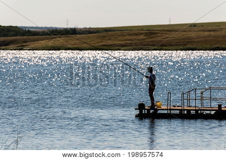 Silhouette of a man who is fishing with a fishing rod on a sunny day