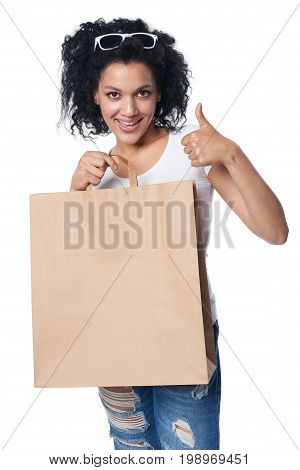 Happy mixed race woman holding craft shopping bag with blank copy space and gesturing thumb up
