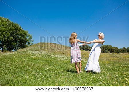 Mother and daughter dancing in a meadow. Young mom and her little daughter holding hands spinnig together.