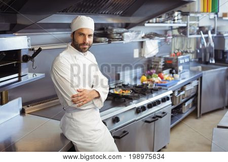 Portrait of smiling chef standing with arms crossed in commercial kitchen at restaurant