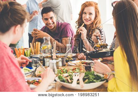 Pretty red haired woman eats breadstick during tasty dinner with vegan friends