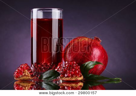 rijpe pomergranate en glas sap op paarse achtergrond