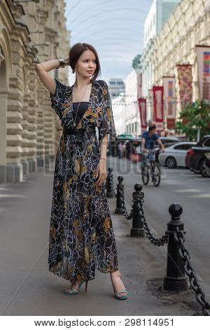 Charming Sensual Woman In Fashionable Gauzy Clothing Is Posing At A Town Street With Cars And People
