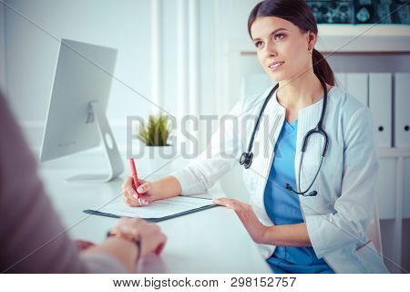 Doctor and patient discussing medical problems in a hospital consulting room. Doc filling in a patient's form