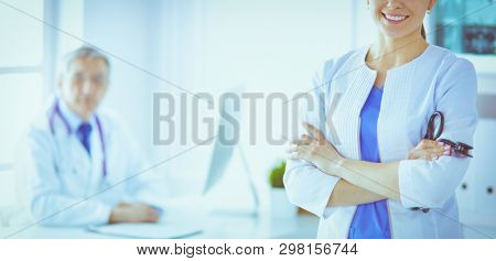 A doctor smiling at the camera with her male colleage in the back of the consulting room in hospital