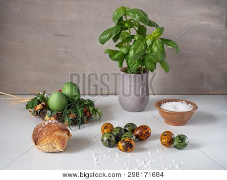 Painted Eggs Of Chicken And Quail Green And Dark Orange On A White Table. Fresh Basil In A Clay Gray