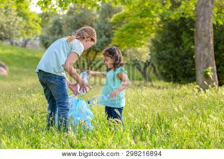 Plastic Pollution On Land. Cildren Picking Plastic Bottle From Grass In Polluted Park.