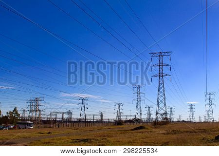 Electricity Pylons Against Blue Sky On Rough Ground