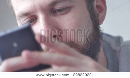 A Young Bearded Man Uses His Mobile Phone. Close-up Shot, Focus On Eyes.