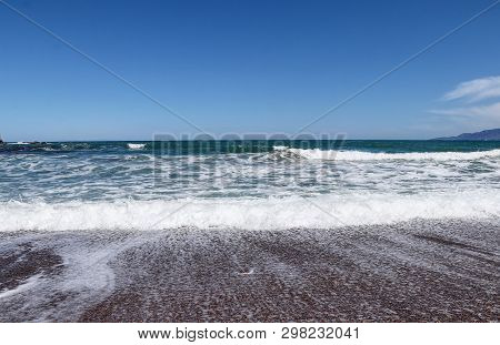 Beautiful Waves On Shore With Foam And Murmur. Mediterranean Sea On Seashore Small City Named Polis,