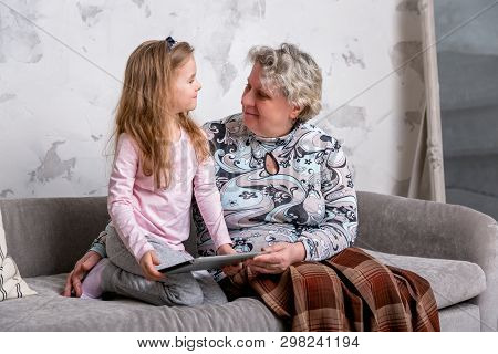 Grandmother And Her Little Granddaughter Are Watching Movies Together And Playing On The Device Whil
