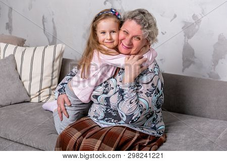 Grandmother And Her Little Granddaughter Are Watching Movies Together And Playing On The Device Whil
