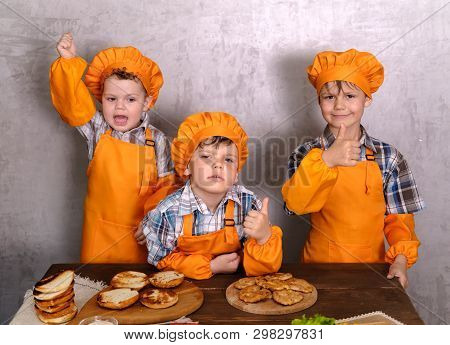Three Cute Boys In Costumes Cooks Engaged In Cooking Homemade Burgers. Three Brothers Preparing Fami