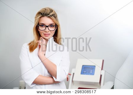 Smiling Confident Female Doctor With Lab Coat On Standing In Her Office With Medical Hardware And Pa