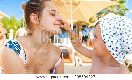 Portrait Of Smiling Happy Toddler Boy Applying Sunscreen Lotion On Mothers Face On Th Esea Beach