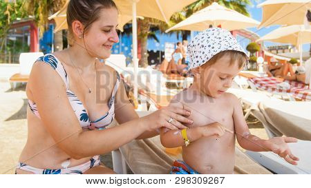 Beautiful Young Mother Using Sun Protection Lotion On Her Childs Sking Before Sunbathing At Sea Beac
