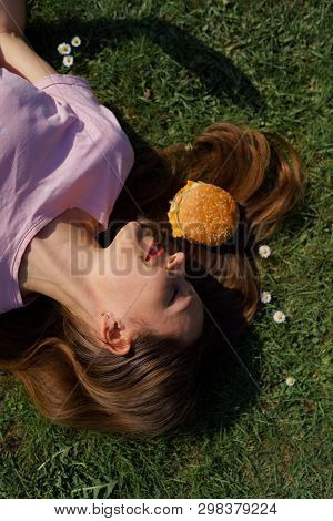 Successful Business Woman Lying On Grass With Fast Food Burger Cheesburger On Hair Enjoying Leisure 