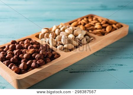 Compartmental Dish With Nuts On Blue Wooden Table. Hazelnut, Almond, Pistachio.