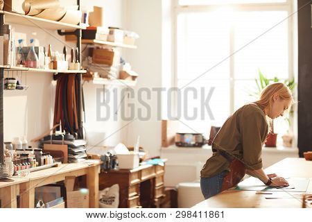 Side View Portrait Of Young Woman Working In Artisan Workshop Lit By Sunlight, Copy Space